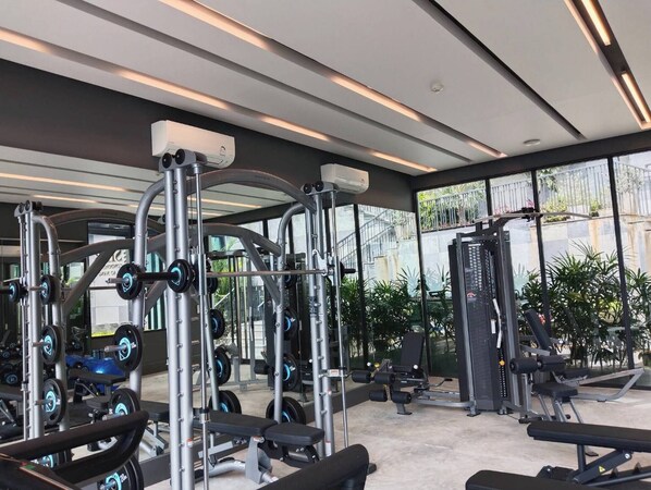 Une salle de sport moderne dotée de divers appareils d’exercice, de grandes fenêtres et d’un intérieur propre et bien éclairé.