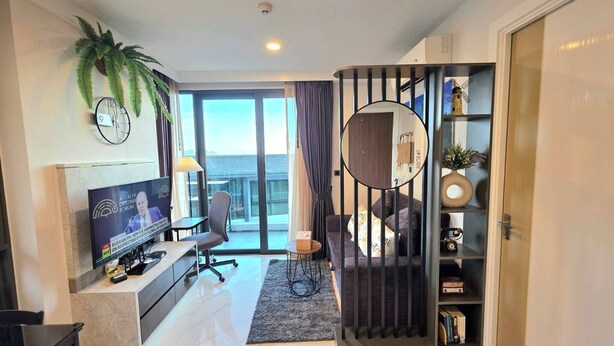 Een moderne woonkamer met een televisie, zitmeubels, een boekenkast en uitzicht op een balkon.