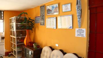 A room with a yellow wall, a glass cabinet, a large plant, framed certificates, and a red door.