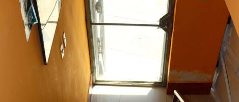 A staircase with alternating red and beige steps, a metal handrail, and a view of the outside through a glass door.