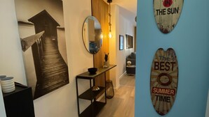 A hallway with a wooden floor, a black console table with a mirror, and a wall with two decorative signs.