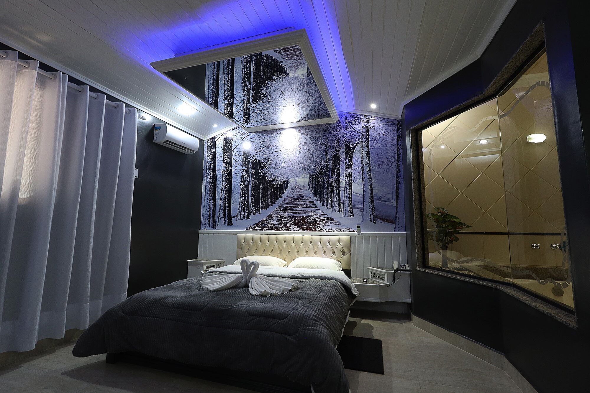 A bedroom with a bed, a wall-mounted air conditioner, and a large window with a view.