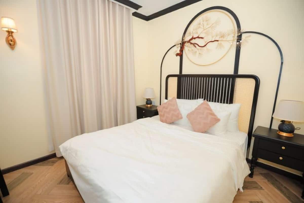 A neatly made bed with white bedding and decorative pillows, a black metal headboard, a wall-mounted lamp, and a nightstand with a lamp.