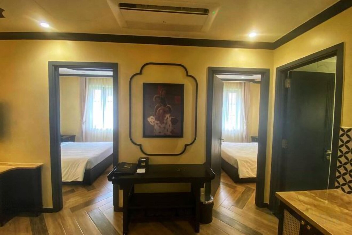 A hotel room with two beds, a desk, and a painting on the wall.