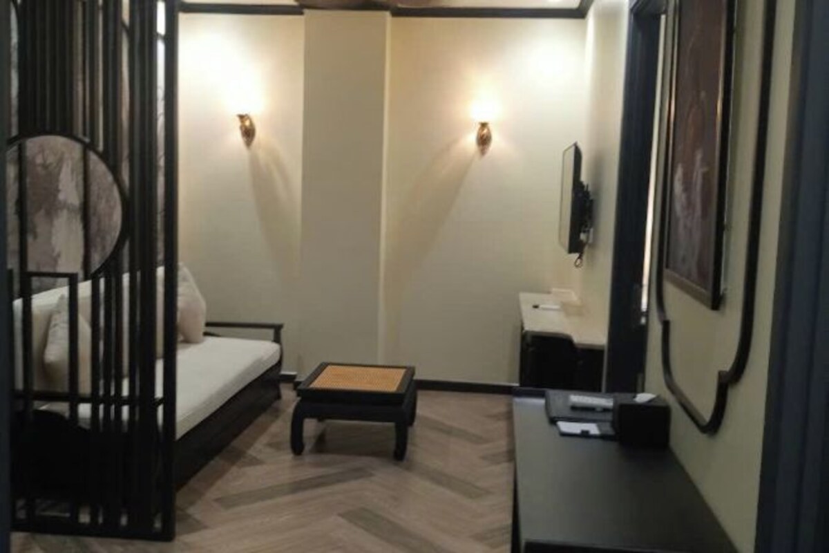 A compact room with a bed, a small table, a desk, and two wall-mounted lights.