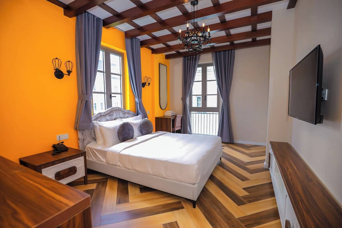 A bedroom with a bed, bedside tables, a desk, a TV, and a window with curtains.
