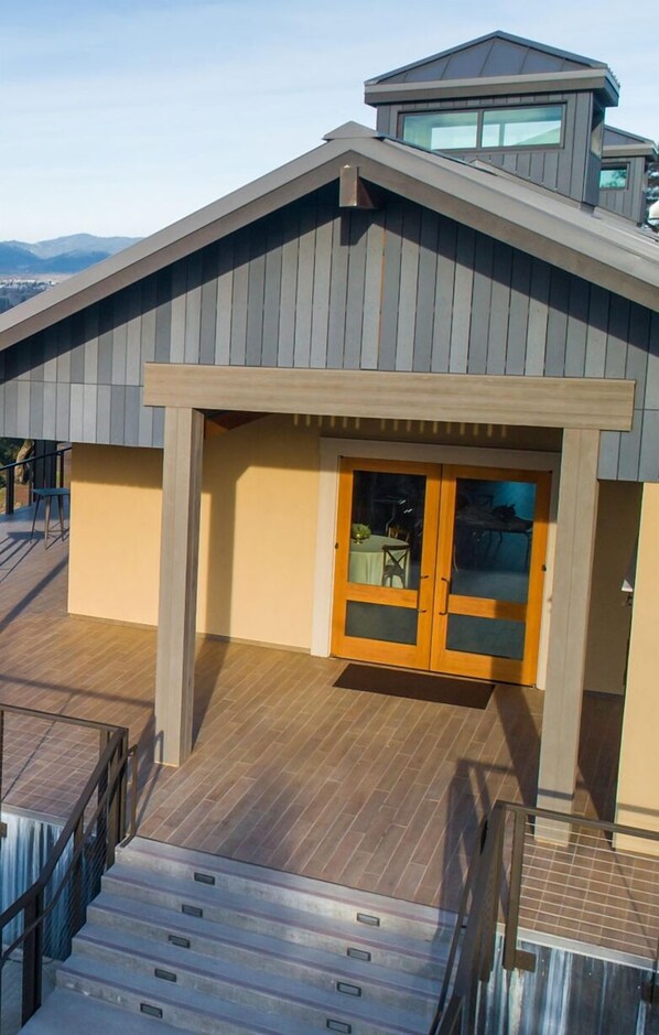 Um edifício moderno com deck de madeira, entrada coberta e escadaria que leva ao nível superior.