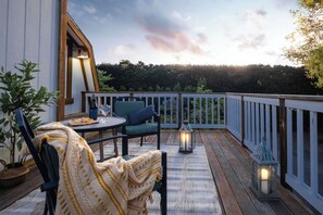 Um terraço ao ar livre com uma mesa e cadeiras, um candeeiro e vista para o céu e árvores.