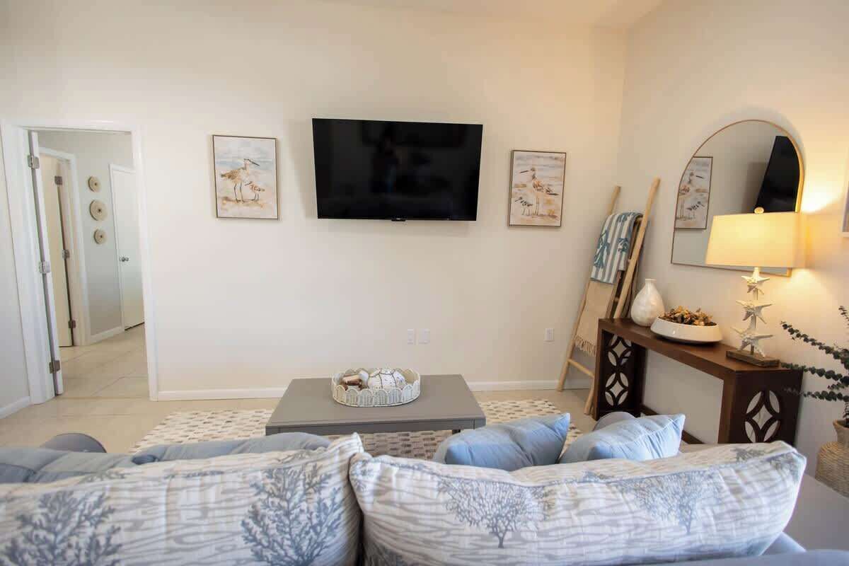 Uma sala de estar com televisão de tela plana, sofá, mesa de centro e mesa lateral com luminária.