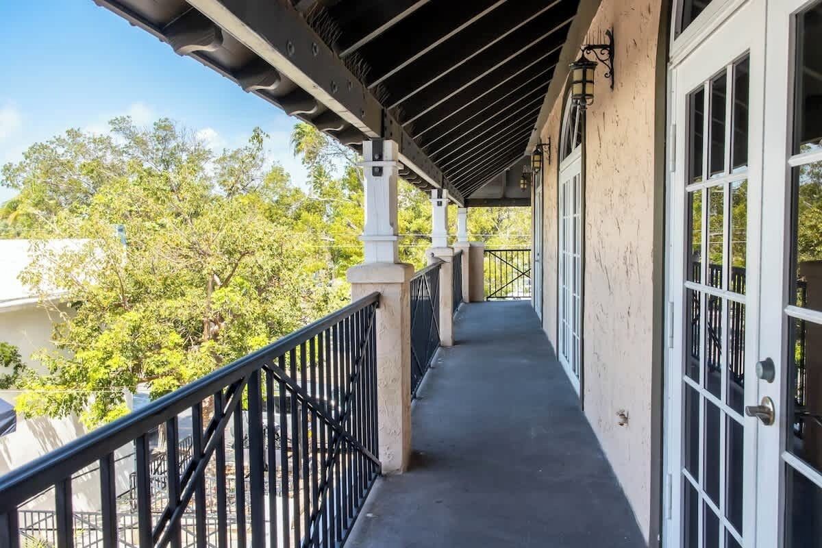 A covered balcony with a railing, a door with glass panels, and a view of trees and buildings in the background.
