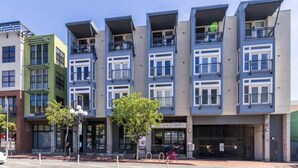 Une rangée d’immeubles modernes à plusieurs étages, dotés de balcons, un café et un portail fermé.