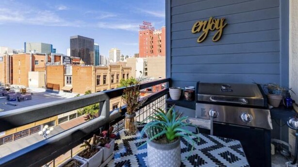 Un balcon avec un barbecue, des plantes en pot et une pancarte sur le mur avec l’inscription « Profitez-en ».