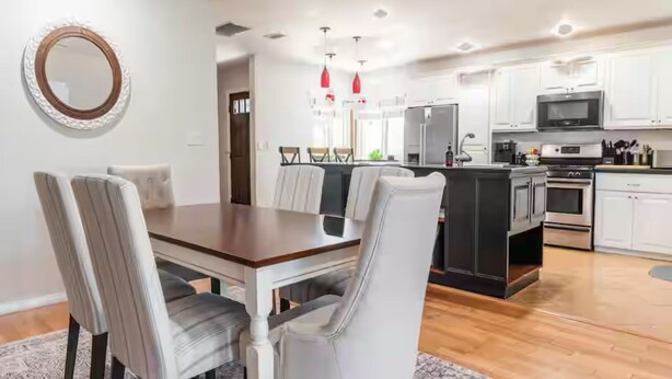 Een moderne keuken met witte kasten, roestvrijstalen apparatuur en een houten eettafel met gestoffeerde stoelen.