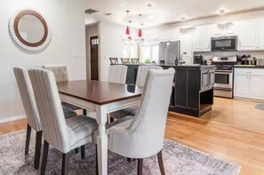 Una cocina moderna con armarios blancos, electrodomésticos de acero inoxidable y una mesa de comedor de madera con sillas tapizadas.