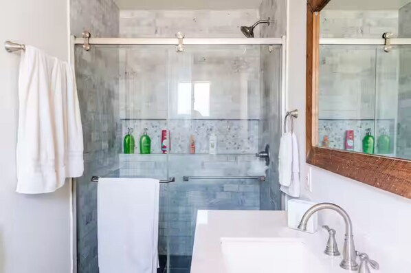 Un baño moderno con ducha envuelta en cristal, un lavabo blanco y un espejo grande.
