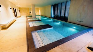 A long indoor swimming pool with a tiled floor, a 1.3m depth sign, and a view of the night sky through large windows. - Royal Executive Living Garden Executive (Caulfield North)