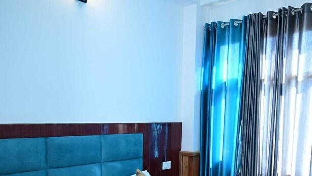 A hotel room with a large bed, a headboard, a nightstand, and a window with curtains. - The Cedar Bliss (Shimla)