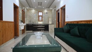 A modern living room with a glass coffee table, a green sofa, and a kitchen area with marble countertops. - The Cedar Bliss (Shimla)