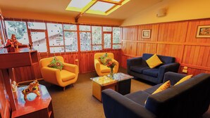 A cozy living room with wooden paneled walls, a skylight, and large windows. There are two yellow armchairs, a blue sofa, and a glass coffee table with a vase of flowers. - CHARMING WOODEN APART IN CENTRAL CUSCO (Cusco)