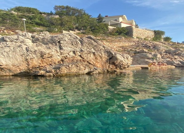 A rocky coastline with clear water, a stone building, and a person relaxing by the water. - Exquisite Studio Apartment by the Beach (Zadar)