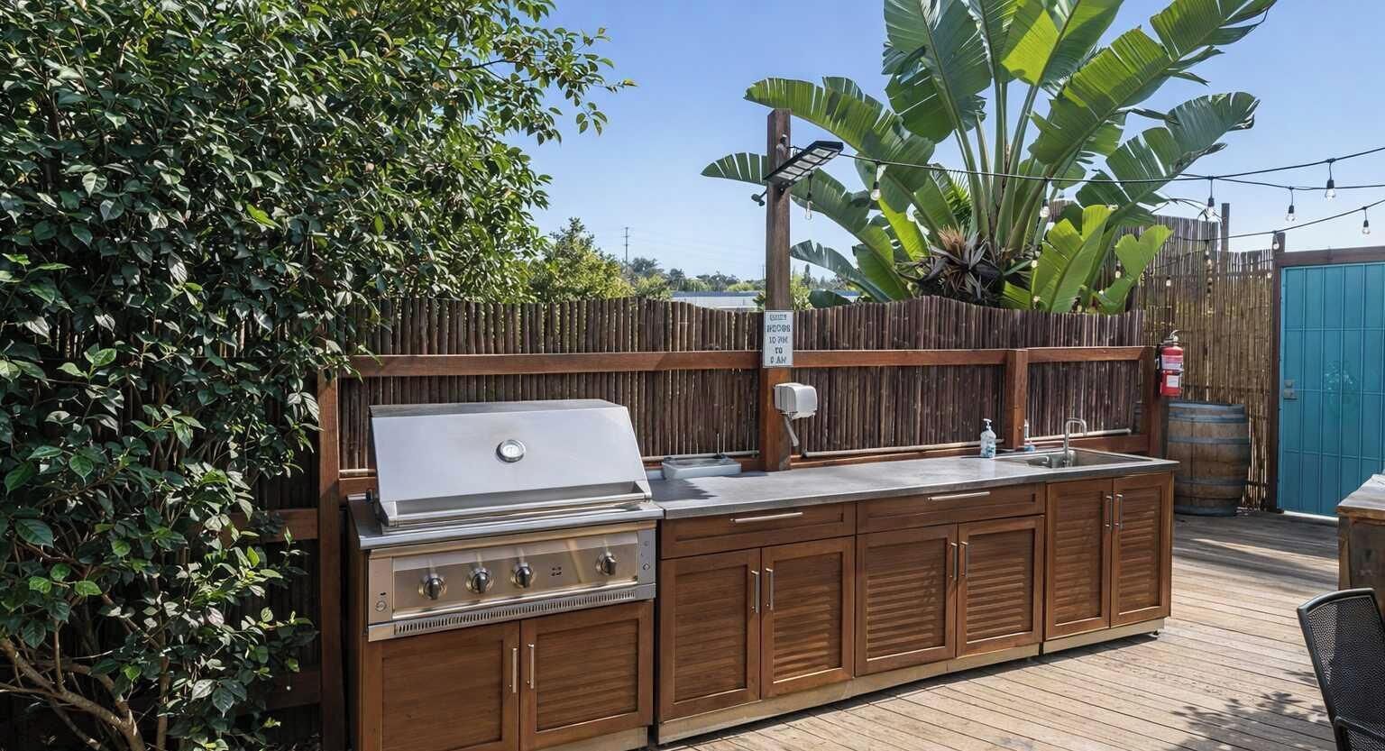 Cucina esterna con barbecue, lavello e pensili in legno.