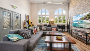 A spacious living room with a grey sofa, wooden coffee table, and a large TV screen displaying a beach scene. - Spacious Private Retreat with Event Spaces (San Diego)