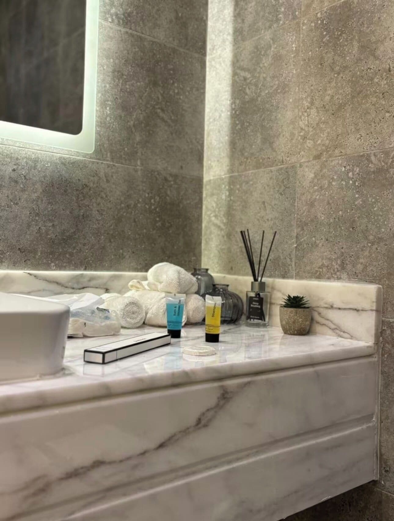 A bathroom with a marble countertop, a white sink, and toiletries.