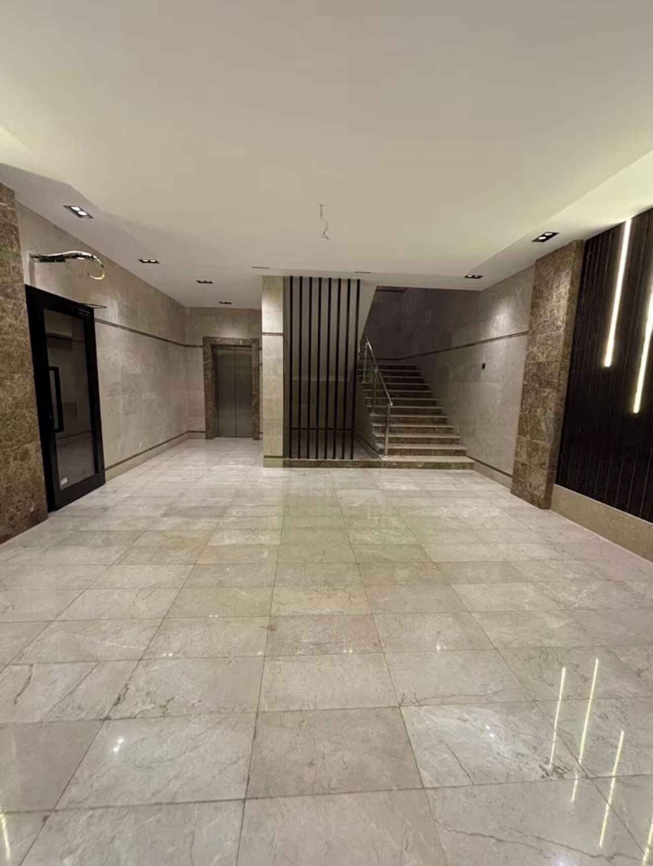 A spacious hallway with a marble floor, a staircase, and a door on the left.