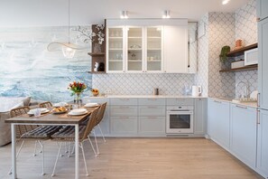 Eine moderne Küche mit weißen Schränken, einem eingebauten Backofen und einem Essbereich mit Tisch für zwei Personen.
