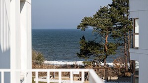 A view of the sea from a balcony with a white building and a pine tree in the foreground. - Perla | Coastal Comfort | Terrace with Sea View | SPA AccessPerla (Gąski)