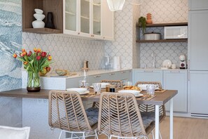 A kitchen with a dining table set for four, wicker chairs, a vase of tulips, and a microwave. - Perla | Coastal Comfort | Terrace with Sea View | SPA AccessPerla (Gąski)