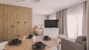 Une chambre d’hôtel moderne dotée d’un coin repas, d’un téléviseur à écran plat et d’une grande fenêtre avec des rideaux.