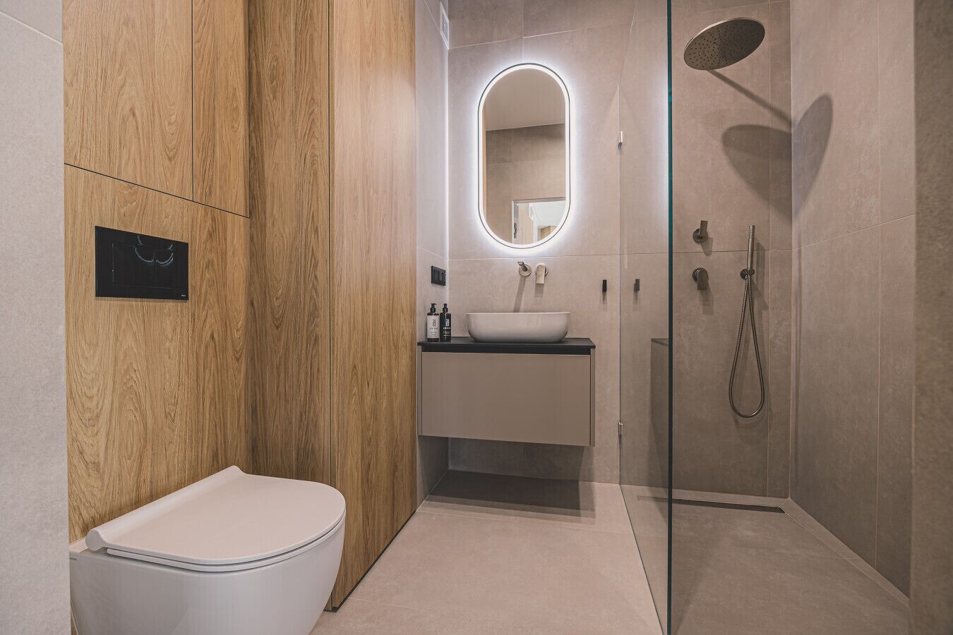 A modern bathroom with a wooden vanity, a white toilet, a glass-enclosed shower, and a mirror with a light.