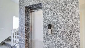 En elevator med en væg af granit, et metalgelænder og et kontrolpanel med to knapper.