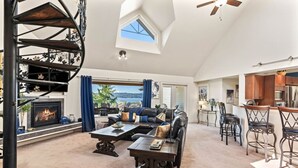 Ein geräumiges Wohnzimmer mit Kamin, einer großen Couch, einem Essbereich mit Barhocker und Blick ins Freie.