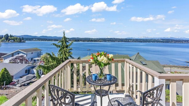 Ein Balkon mit Blick auf einen See und Berge, ausgestattet mit einem Tisch, Stühlen und einem Blumenstrauß.