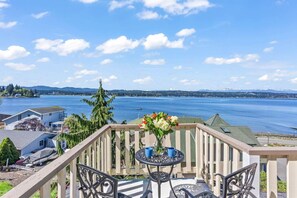 Un balcon offrant une vue sur un lac et des montagnes, avec une table, des chaises et un vase de fleurs.