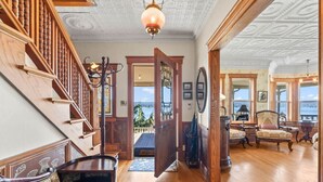 Ein prachtvoller Eingangsbereich mit einer Holztreppe, einer großen offenen Tür, die auf einen Balkon führt, und einer Sitzecke mit Möbeln im Vintage-Stil.