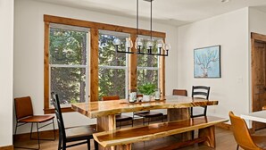 Un espace repas avec une table et des bancs en bois, de grandes fenêtres et un luminaire suspendu.