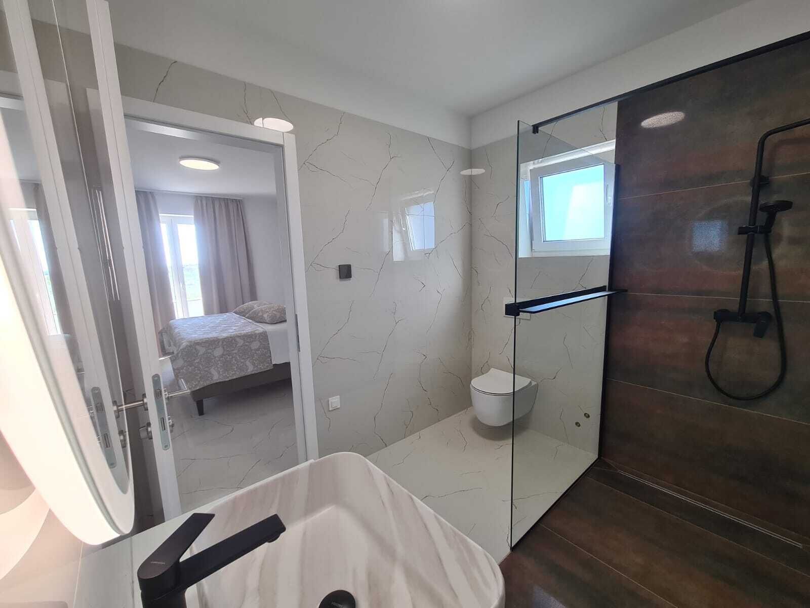 A modern bathroom with a glass shower enclosure, a toilet, and a sink.