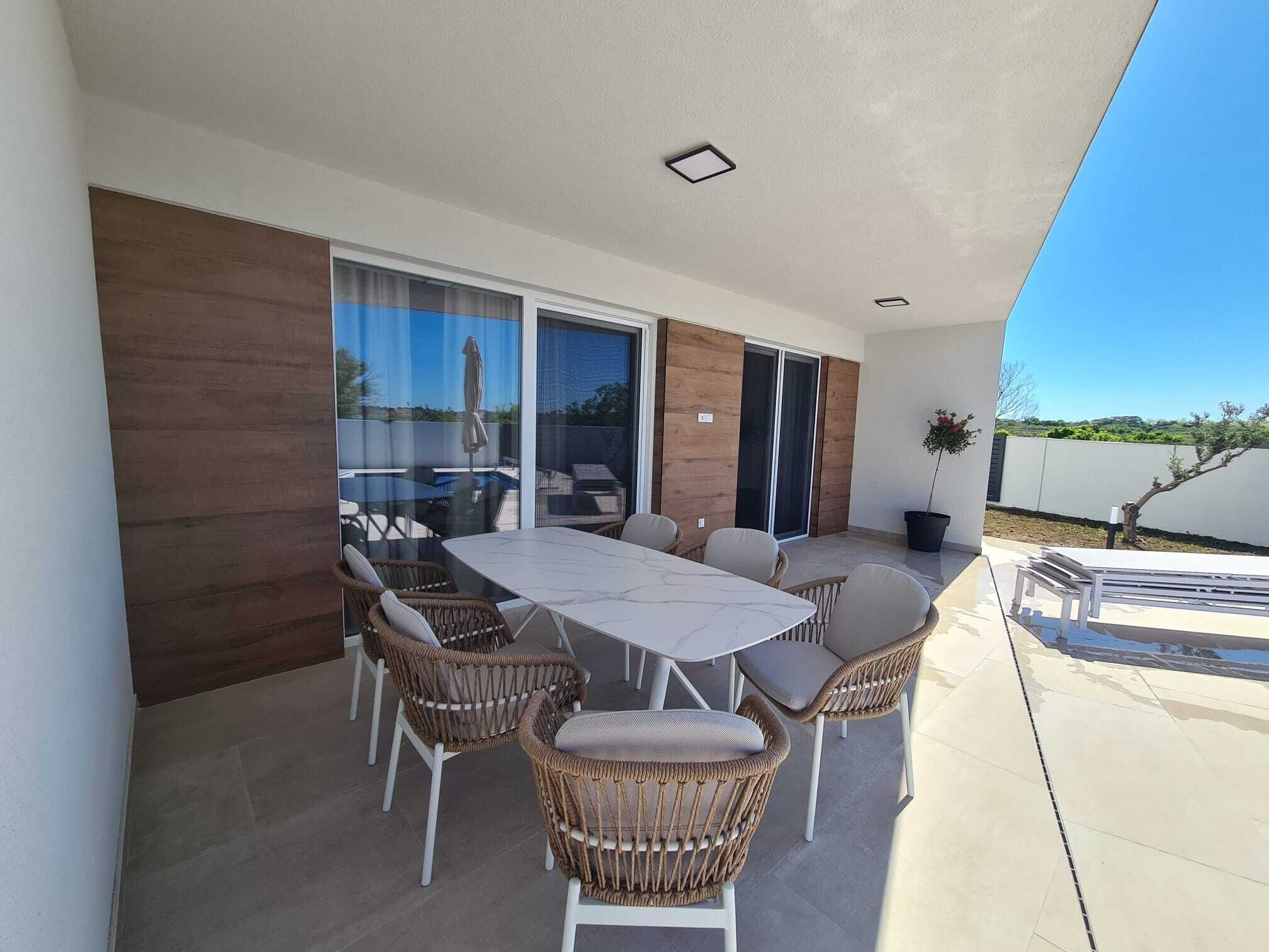 Une terrasse avec une table et des chaises, de grandes fenêtres et une vue sur le paysage.