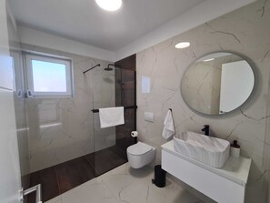 A modern bathroom with a glass-enclosed shower, a white toilet, a vanity with a mirror, and a large round mirror on the wall. - New villa Angelo 2025 ( family and pet friendly) (Privlaka)