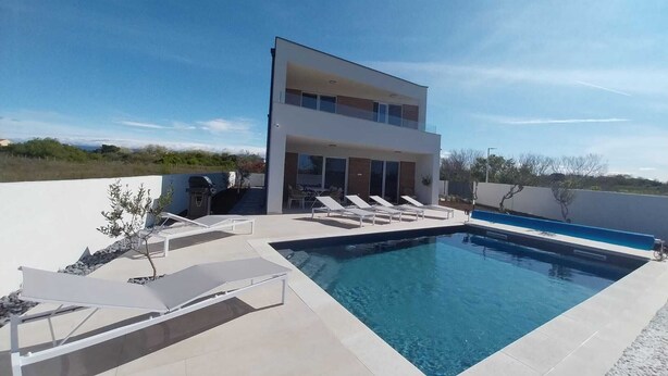A modern two-story house with a swimming pool, outdoor seating, and a clear view of the surrounding landscape. - New villa Angelo 2025 ( family and pet friendly) (Privlaka)