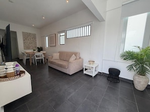 Un salon moderne avec un canapé, une table à manger et des chaises. On y trouve une petite table d’appoint sur laquelle est posé un bol.