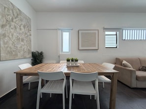 Un coin repas avec une table en bois et des chaises blanches, un canapé et une plante en pot.