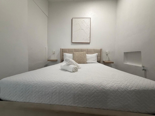 Un lit bien fait, avec une couette blanche matelassée, deux oreillers et des serviettes enroulées posées sur le lit.