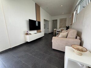 A modern living room with a flat-screen TV, a sofa, a small table, and a basket.