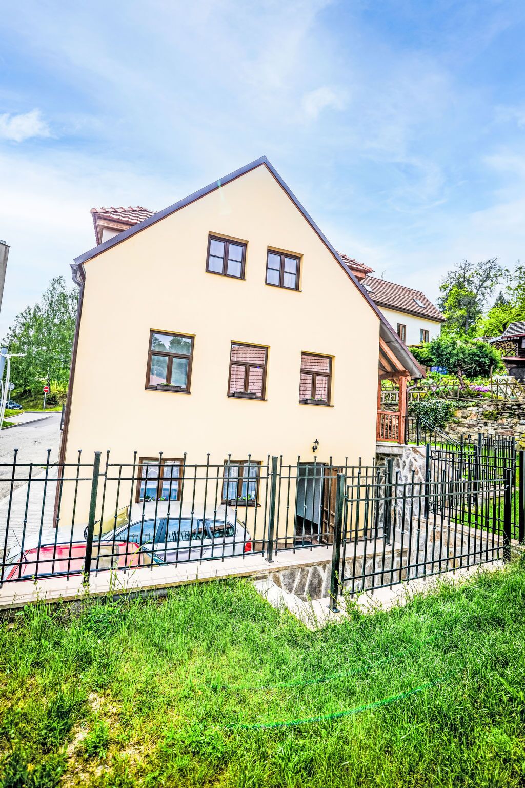 Ein zweigeschossiges Gebäude mit einer beigefarbenen Fassade, einem geneigten Dach und einem schwarzen Metallzaun im Vordergrund.