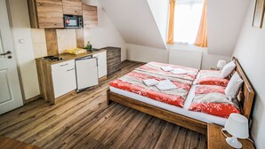 A bedroom with a wooden bed, a small kitchenette, and a window with curtains.