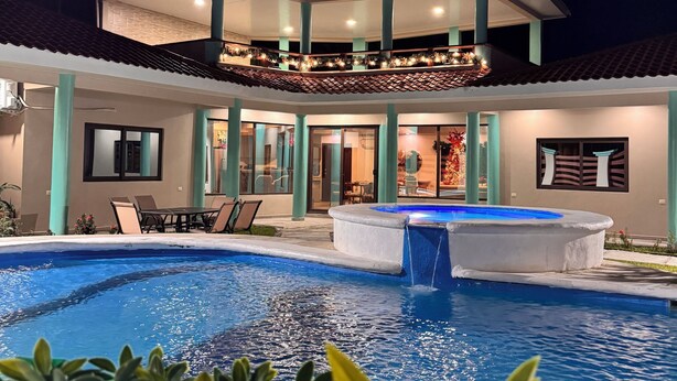 A modern house with a swimming pool, a covered patio, and a balcony with lights.